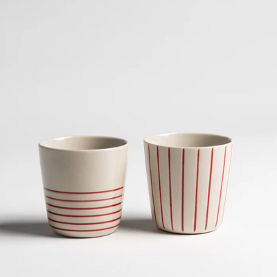Two ceramic cups with red stripes on a light gray background