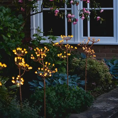 Solar powered LED fennel stake light along a pathway next to shrubbery