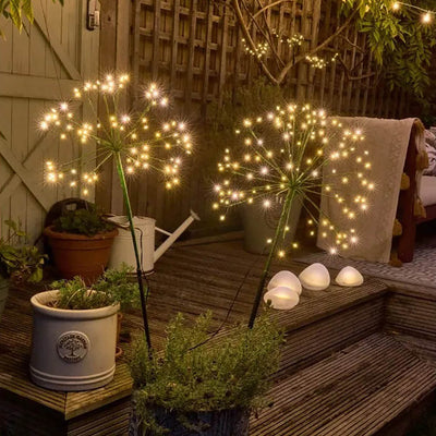 Two solar powered LED stake lights in a dandelion design placed in a plant pot on a wooden patio area