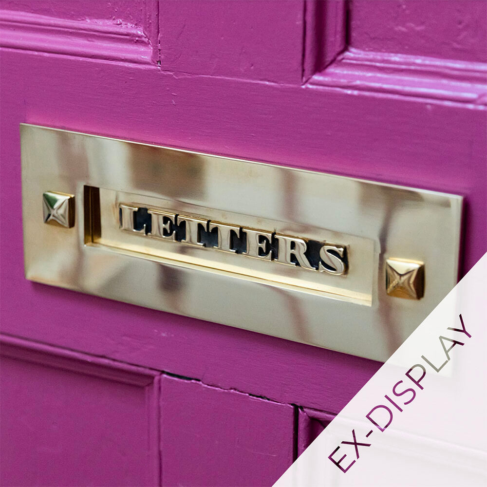 Solid brass classic letterplate without clapper with the word letters on the flap, fitted to a deep pink door and an ex-display watermark on the image