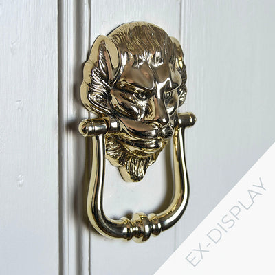 Solid brass lions head door knocker on a side angle on a pale grey door with a watermark and ex display text in the corner