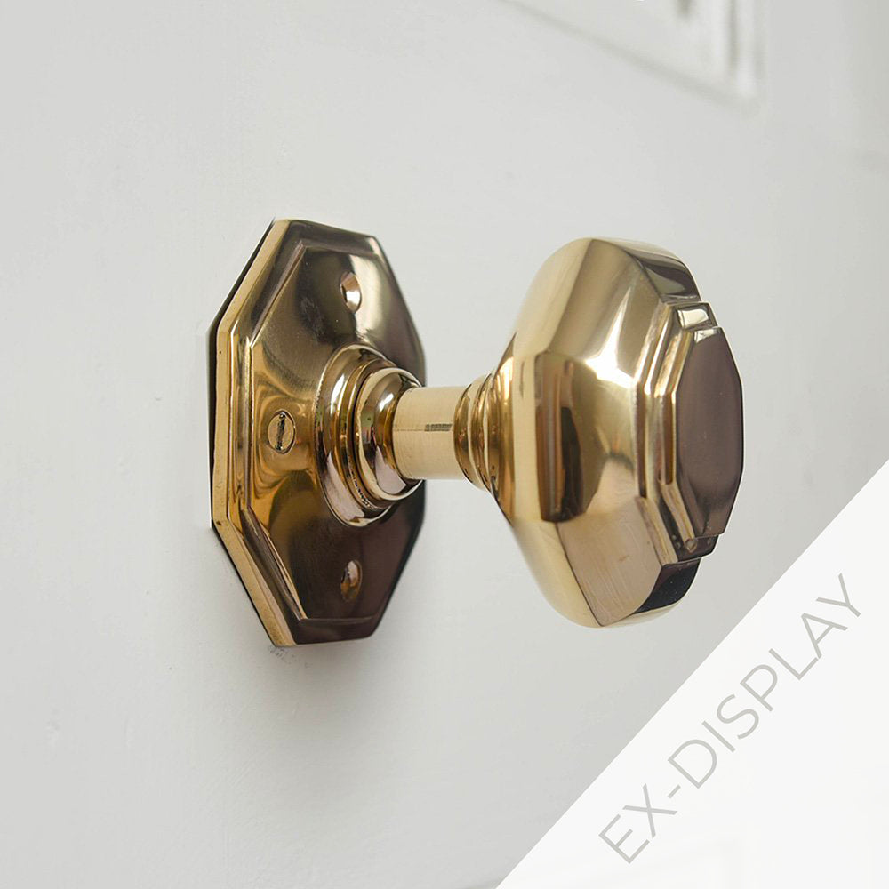 Polished brass octagonal door knob on a pale grey background with a watermark and ex display text in the corner