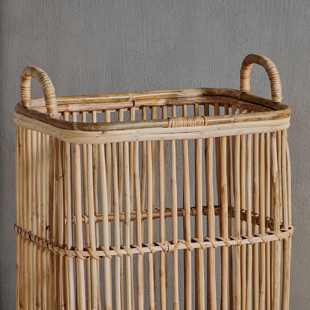 Close up of a rattan laundry basket with handles against a dark grey wall