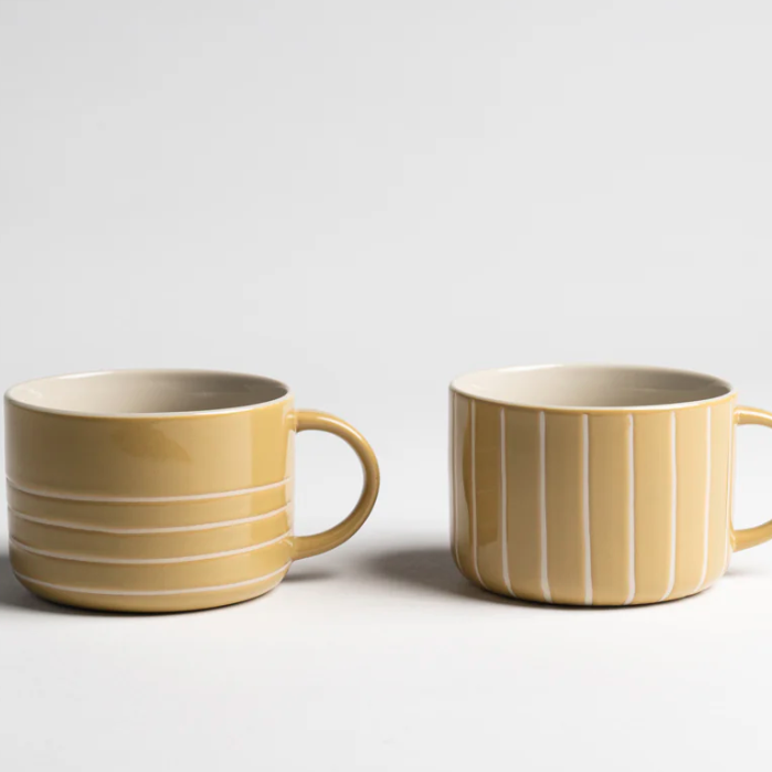 Two yellow ceramic mugs with white stripes on a light gray background