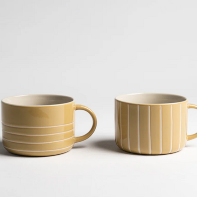 Two yellow ceramic mugs with white stripes on a light gray background