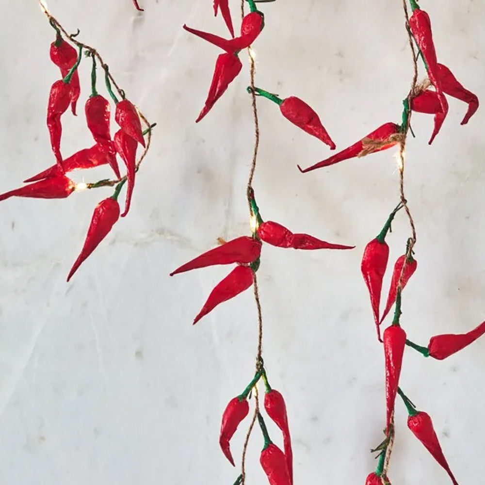 Red chilli pepper paper LED string lights hanging on a natural brown string against an off white wall