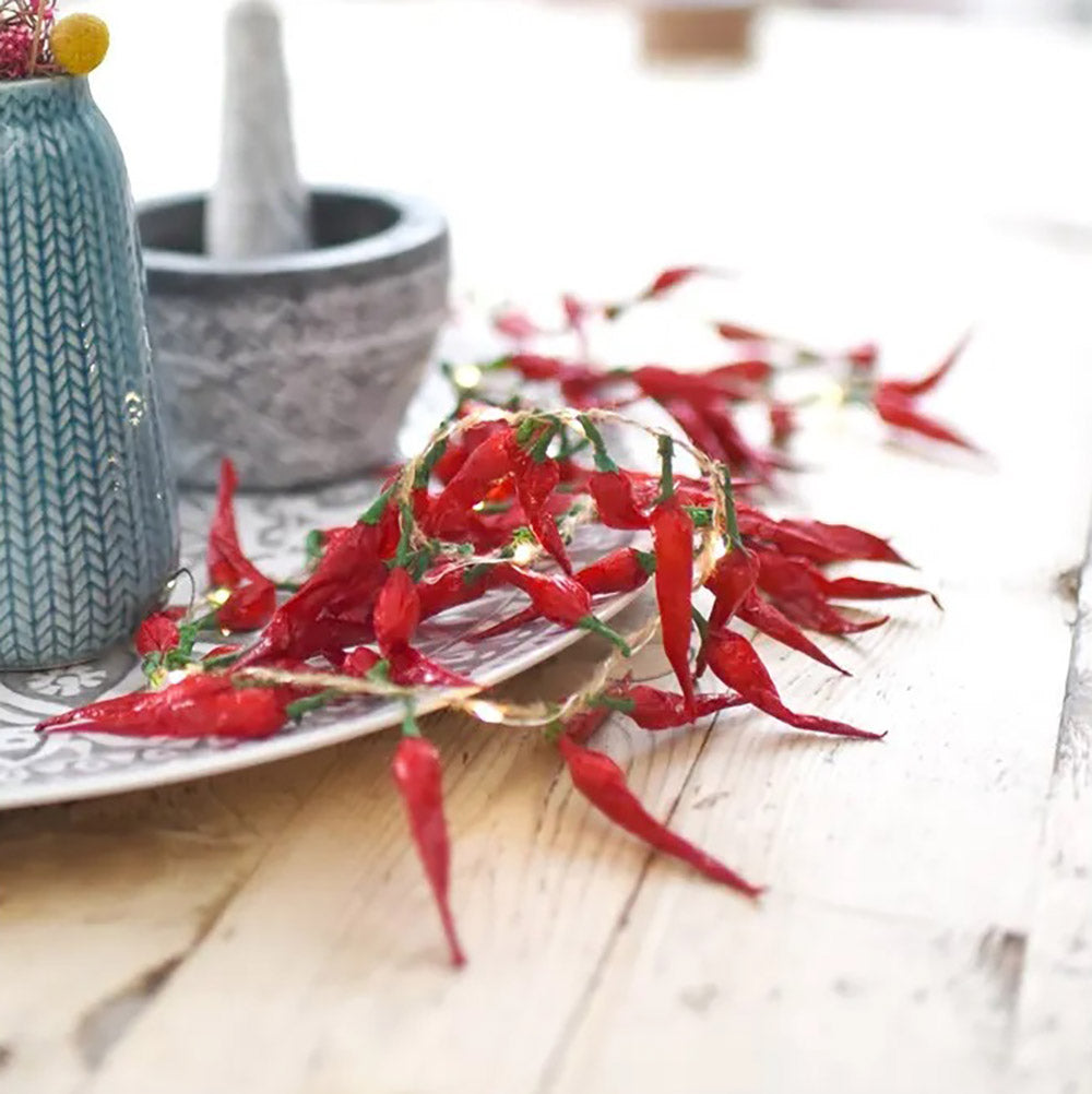 Red chilli paper fairy lights with warm white LED lights placed on a china plate on a wooden kitchen table with a pestle and mortar in the background