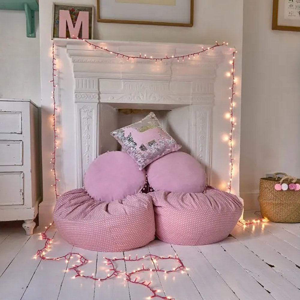 Warm white led fairy lights with a pink cable hanging over a disused fireplace with pink ban bags and pink cushions in front
