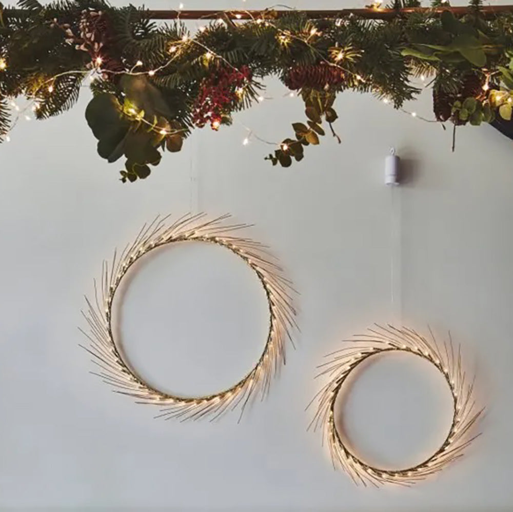 Warm white LED fairy light in a hooped design with wire spokes around the outer edge. The small and large size next to each other on a white wall with a christmas garland hanging above.
