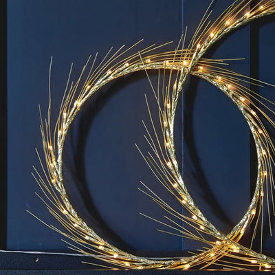 Warm white LED fairy light in a hooped design with wire spokes in a circular design around the edge. Small and large size next to each other leaning against a dark blue background