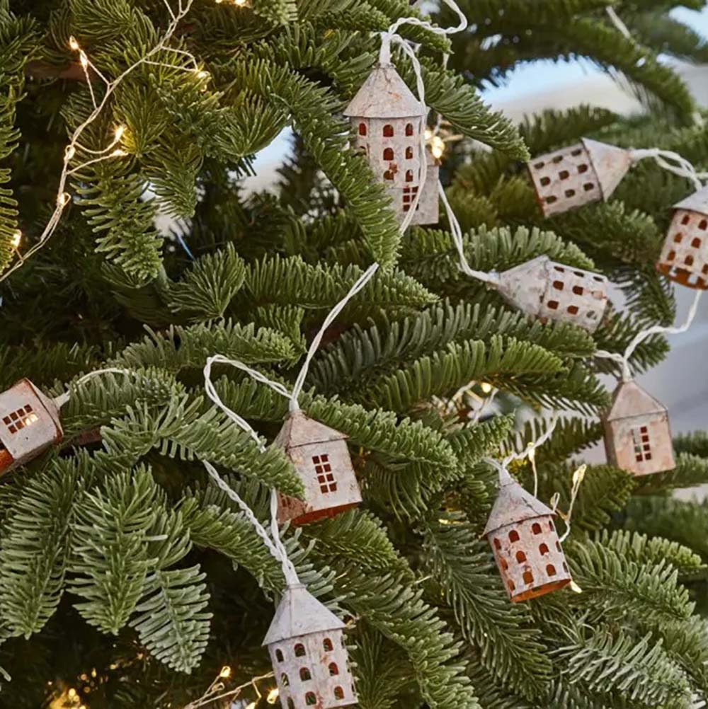 Warm white LED string lights featuring rustic white metal village type houses hanging from white wire on a christmas tree