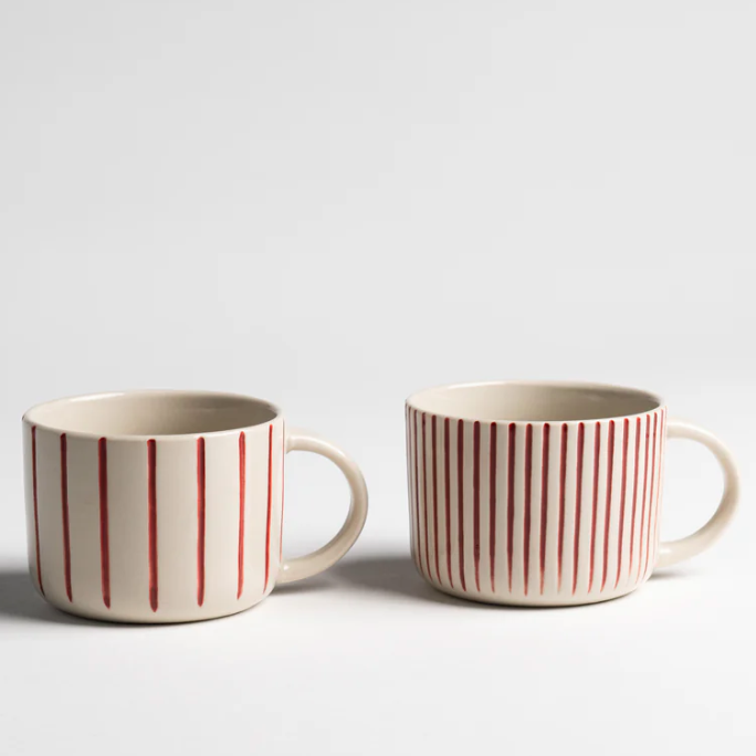 Two ceramic mugs with red vertical stripes on a light gray background