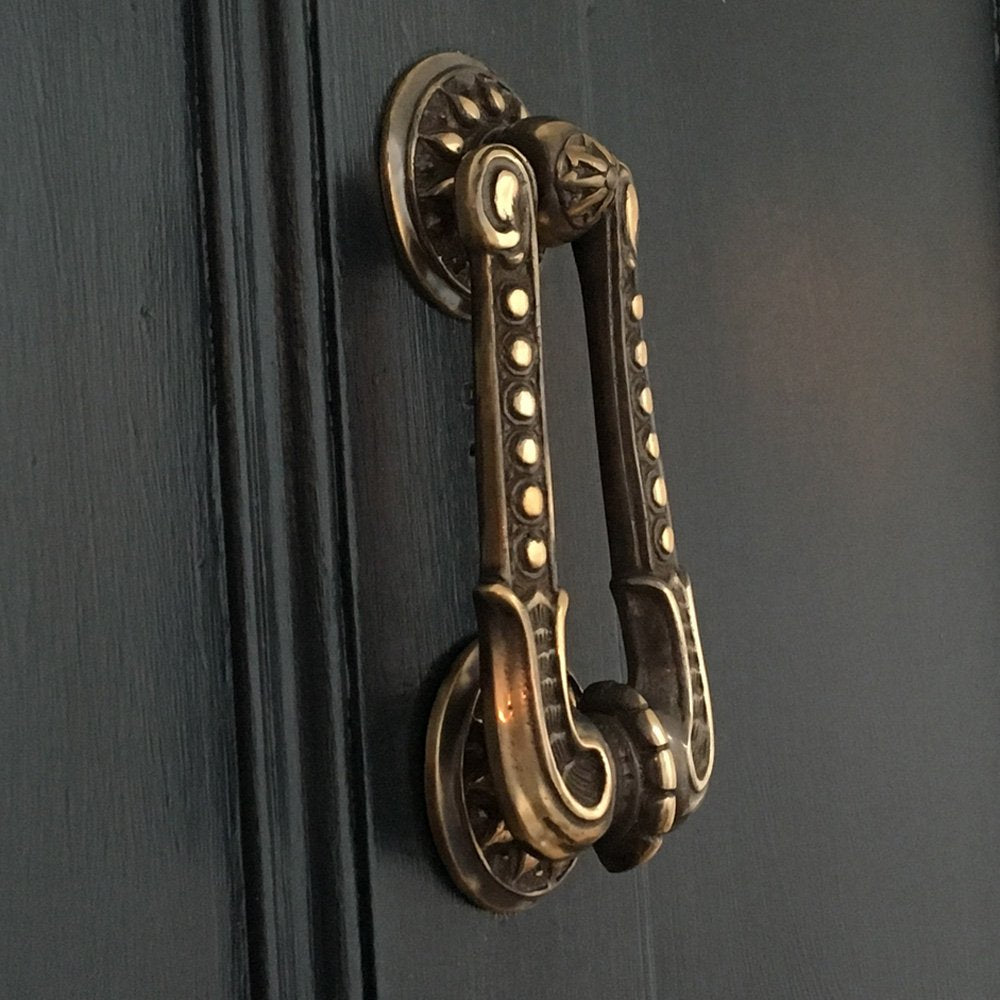 Aged brass regency style door knocker on dark background