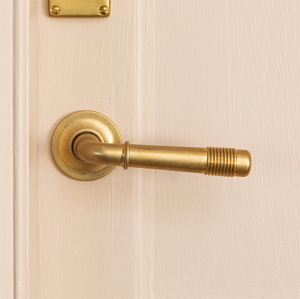 Crest lever handles with reeded beehive detailing on a pink door. Seen here in aged brass - British made