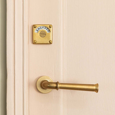 aged brass grace lever handles and indicator bolt on pink door