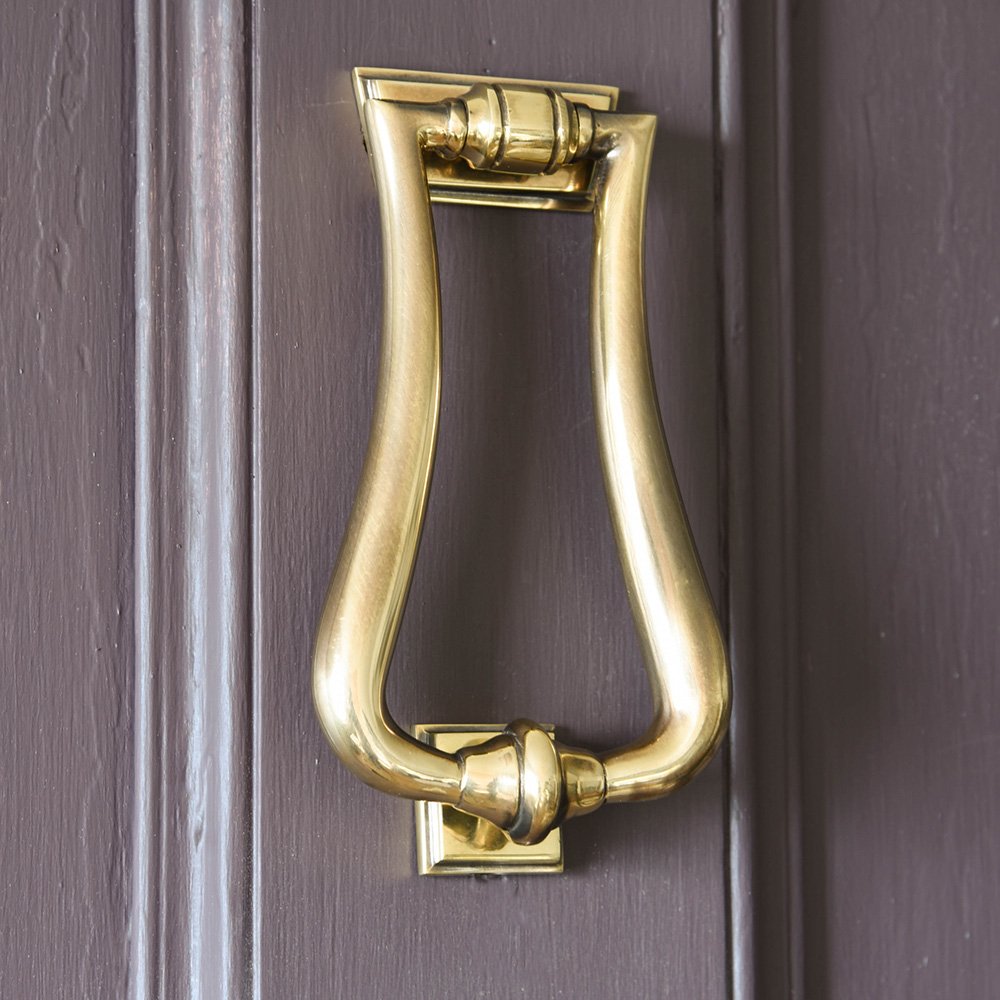 An art deco style door knocker in an aged brass finish fitted to a door