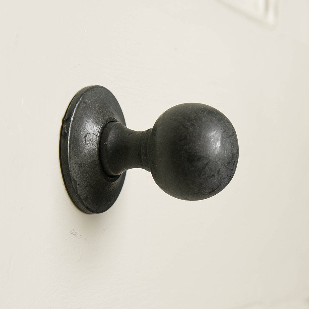A round door knob in black beeswax finish showing the concealed backplate fitting
