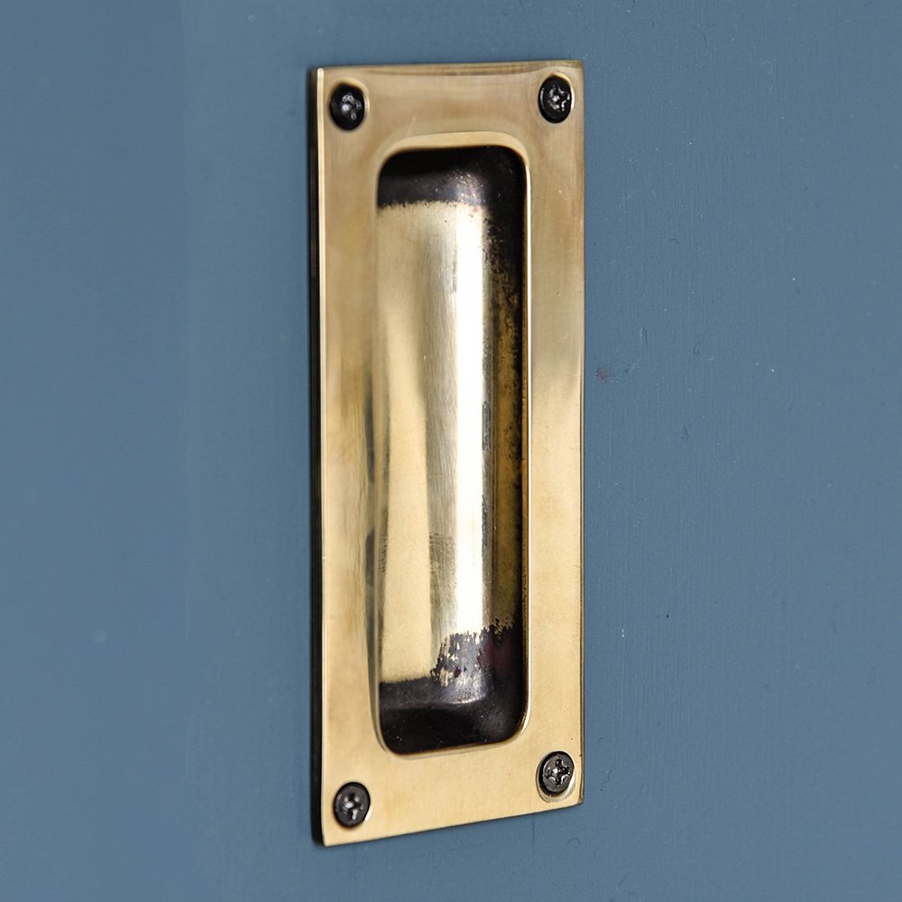 A flush door handle fitted to a cupboard showing the aged brass finish