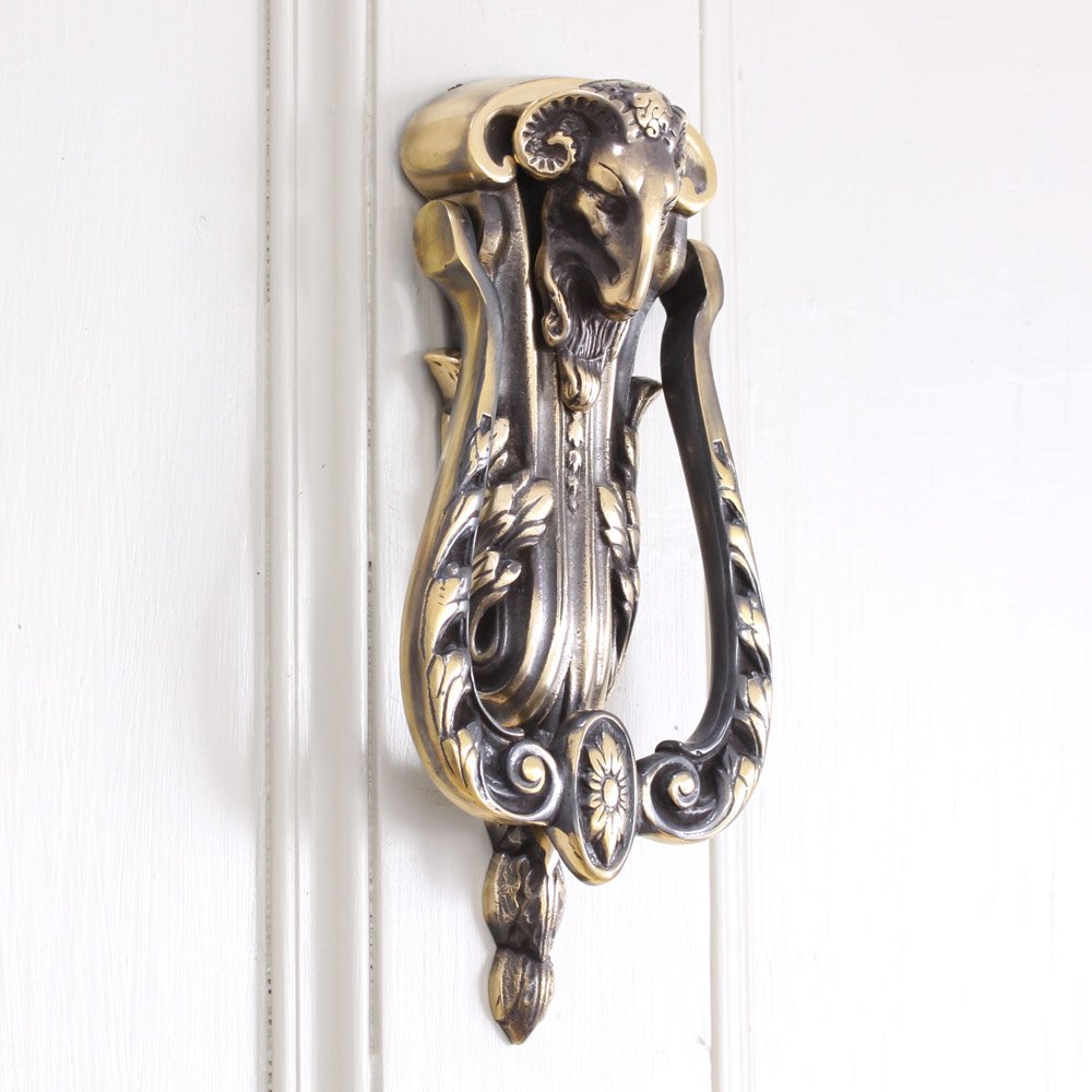 Aged brass rams head door knocker on white door