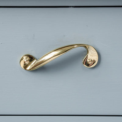 A Twisting Cupboard Handle in Polished Brass fitted horizontally to a cupboard door