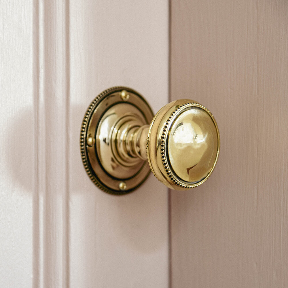 Beaded edge door knob in brass on a pink door