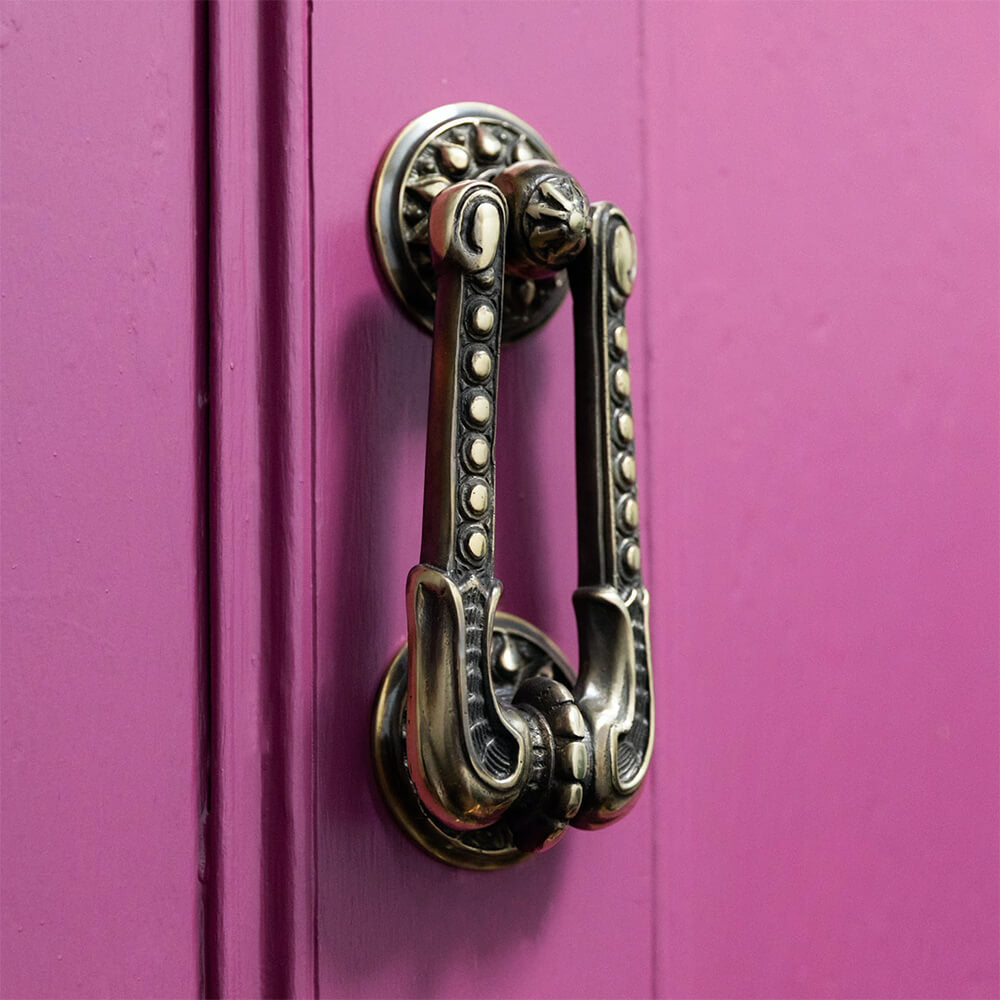 Aged brass regency styl door knocker on a bright punk front door