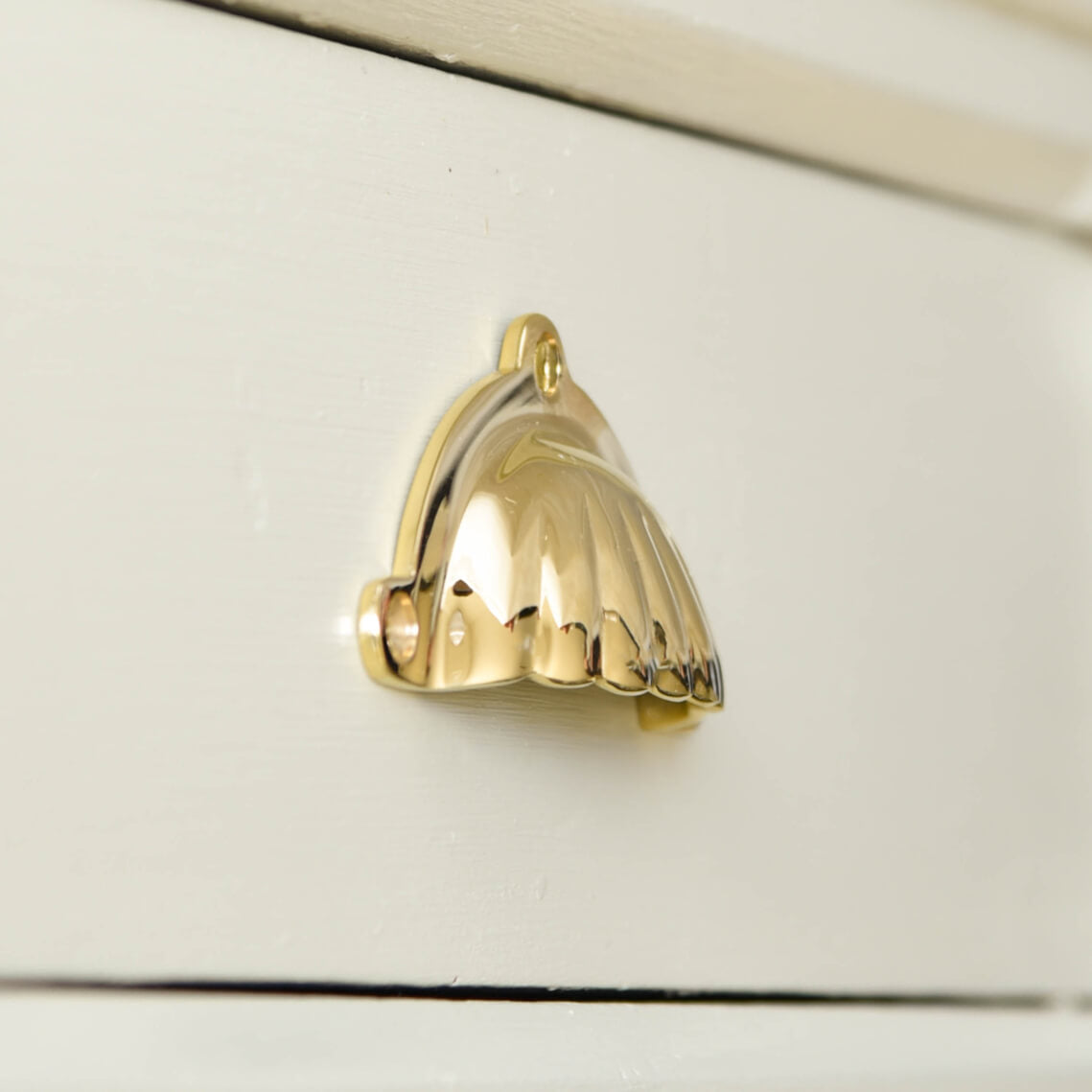 scalloped brass drawer pull seen in profile on beige drawers