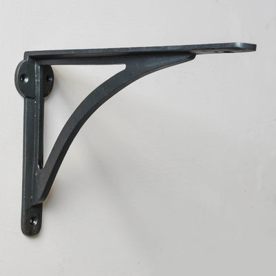 A curved shelf bracket in a black beeswax finish fitted to a wall