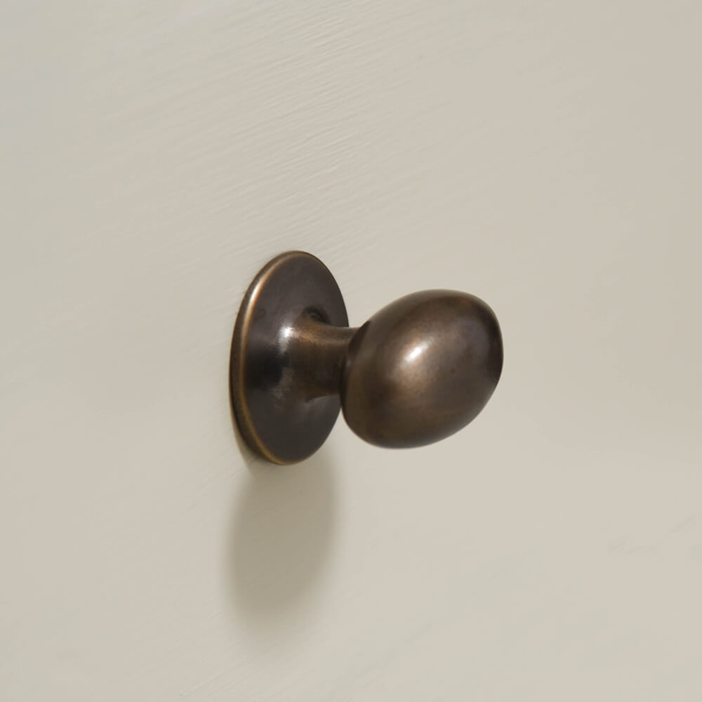 oval cabinet knob on cream drawers in distressed antique brass which is a living finish - shown on an angle