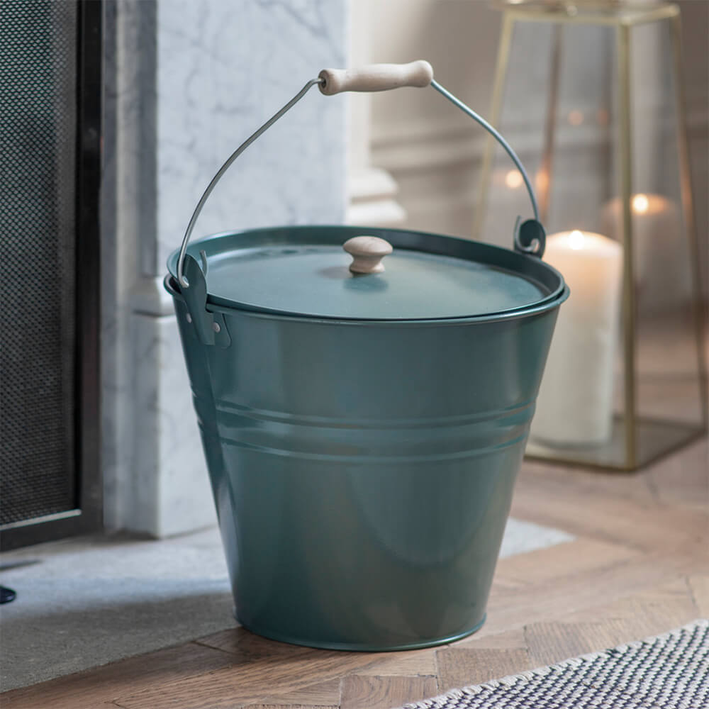 Forest green coloured fire bucket with lid beside a fireplace