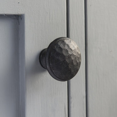 A forged black beaten cabinet knob fitted in situ to a cupboard door