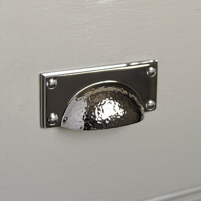 A drawer pull fitted to a cupboard door showing the hammered polished nickel finish