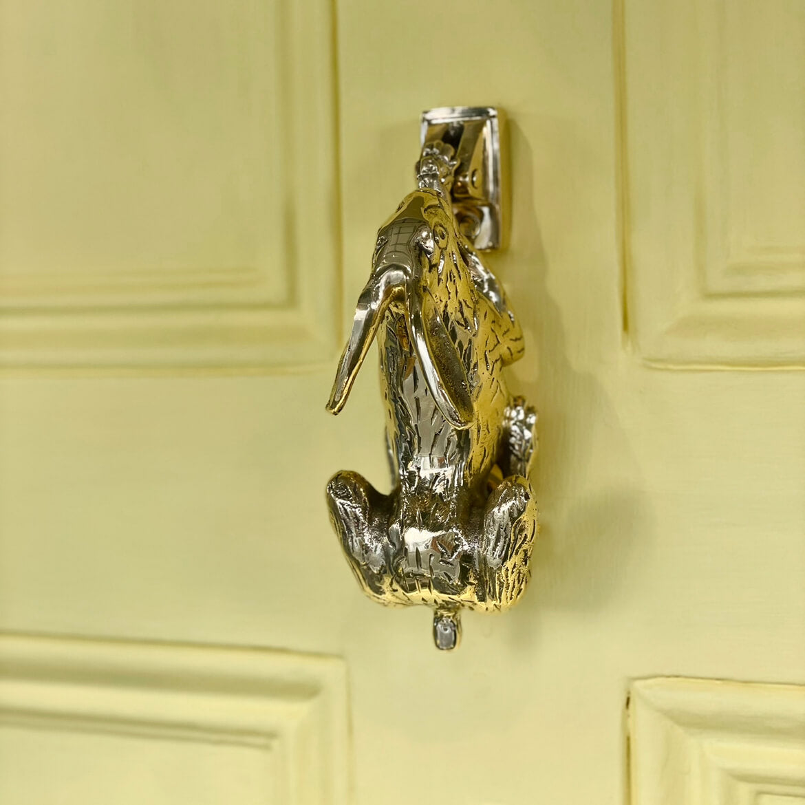 Brass Hare door knocker on yellow door seen front above