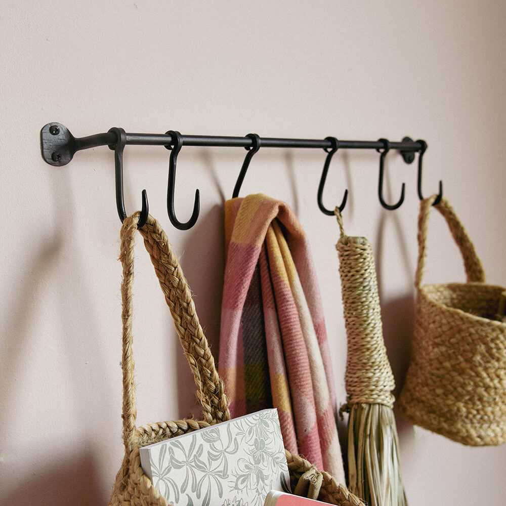 Ikoma Hook Rail in black with blankets and baskets hung from it against a pink wall