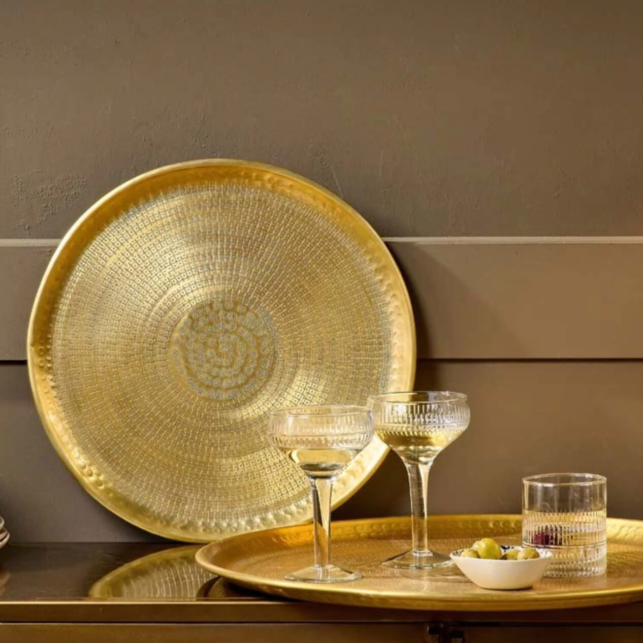 Brass trays in two different sizes used to hold drinks and as decoration against a wall.