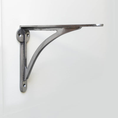 A curved shelf bracket in natural iron fitted to a wall