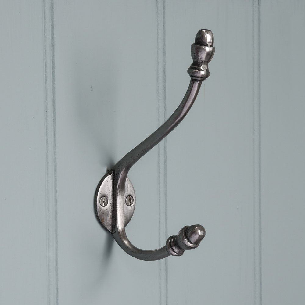A double coat hook in a smooth natural iron finish fitted to a wall