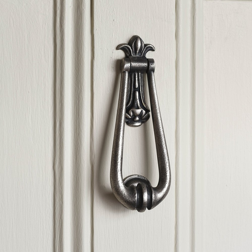A looped door knocker with decorative backplate in a pewter finish