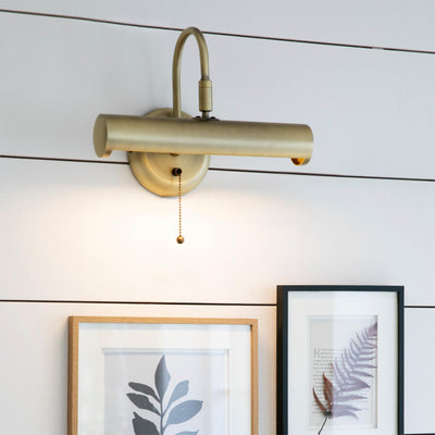 Picture light with brass finish seen on a panelled wall - lit