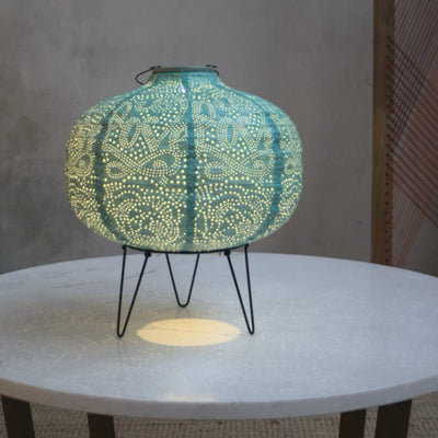 Teal lantern seen lit on a stand on a side table