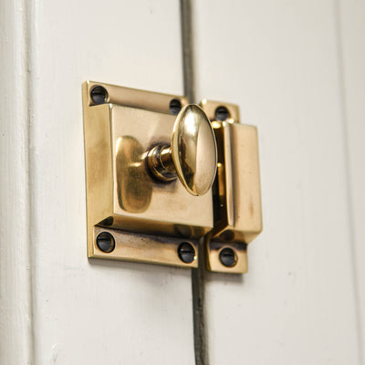 A Sprung Oval Cabinet Latch in an aged brass finish fitted to a cupboard door