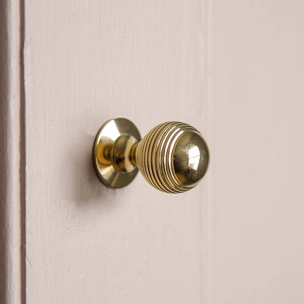 Reeded Beehive Cabinet Knob in Polished Brass on pale pink cupboard door.
