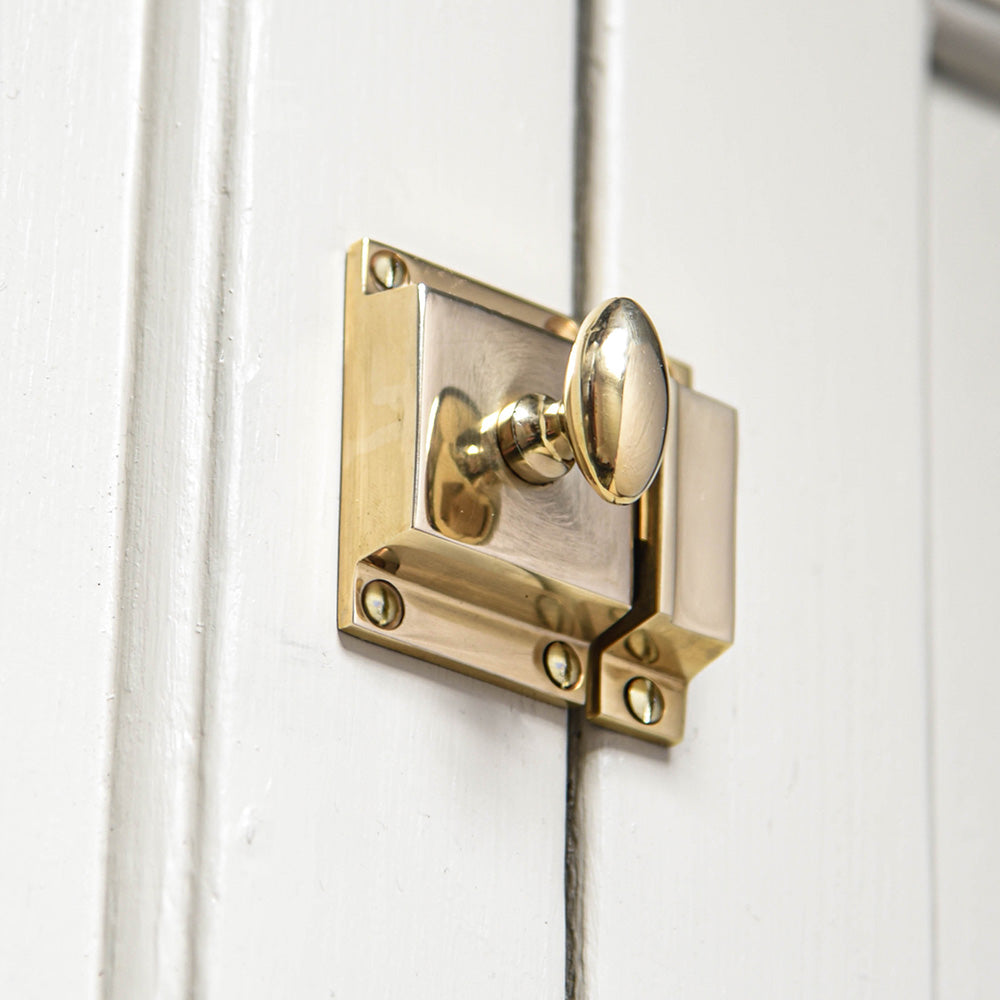 An Oval Cabinet Latch in a polished brass finish fitted to a cupboard door