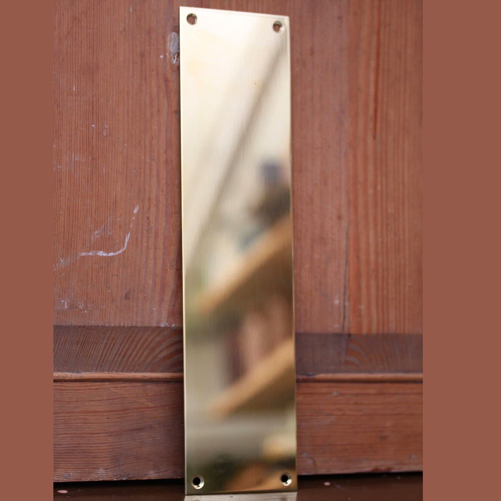Polished Brass Plain Fingerplate leaning on wooden door.