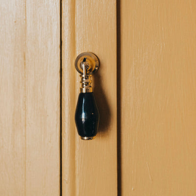 Brass and black ceramic drop pull on yellow cupboard front on