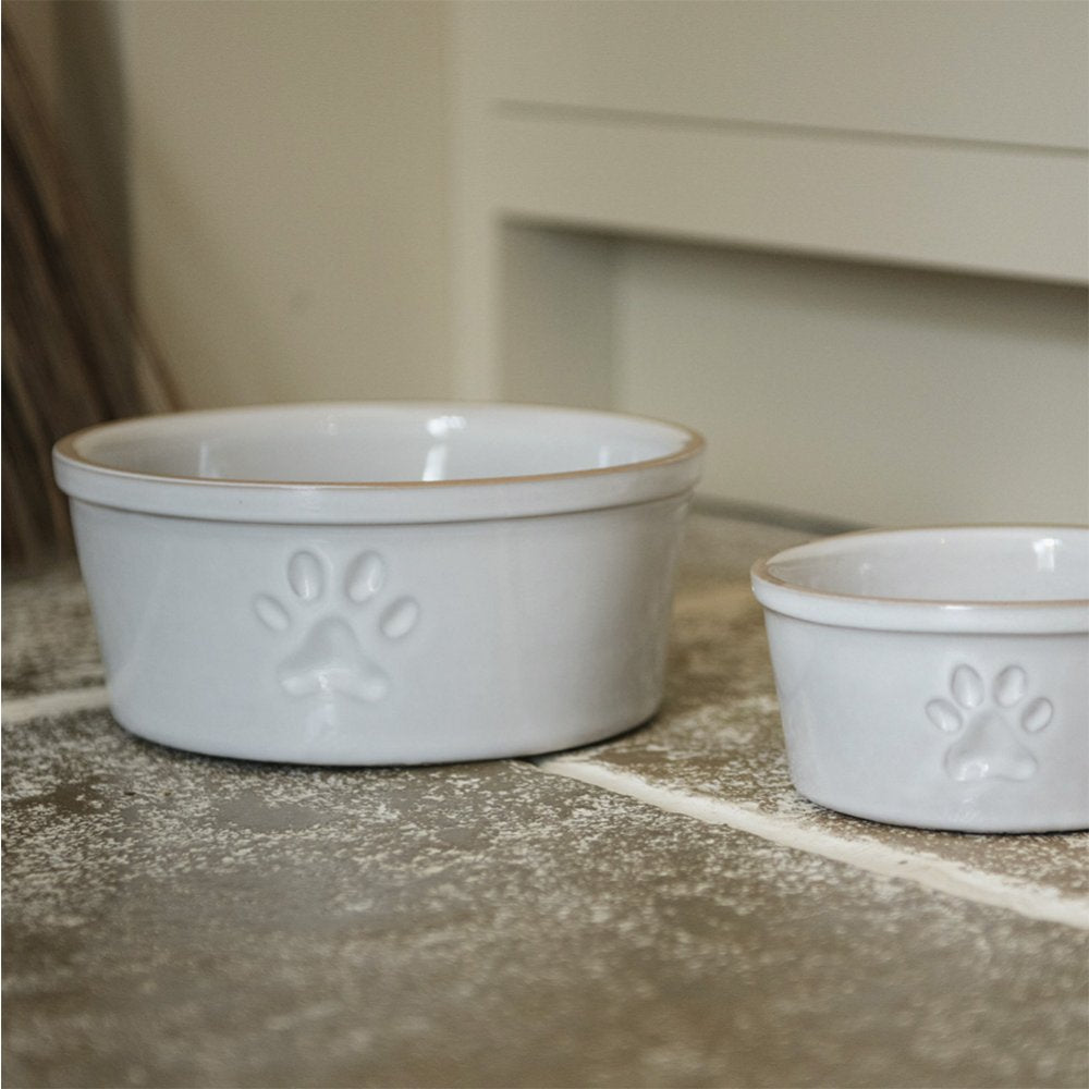 Close up of large (left) and small (right) ceramic pet bowls in white with single paw print design