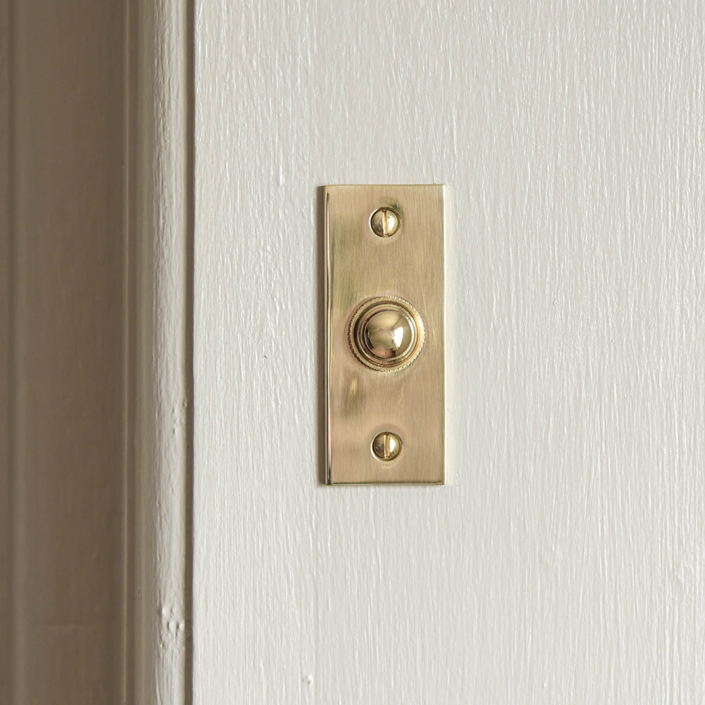 Front view of solid unlacquered Rectangular Brass Bell Push on white door
