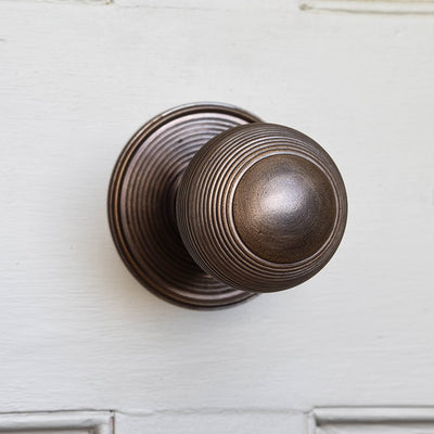 Front view of solid brass Large Beehive Door Pull with distressed antique brass finish on white door.