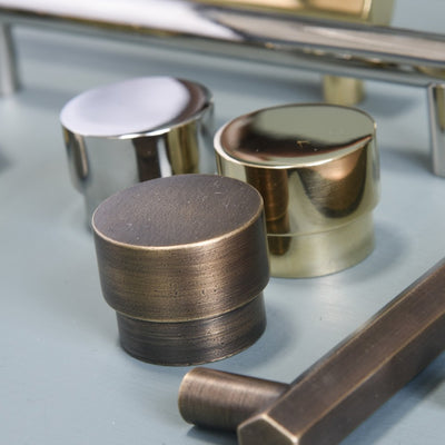 Variants of Drum Cabinet Knob with polished nickel (left), distressed antique brass (center) and polished brass (back, right).