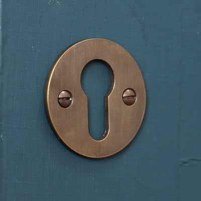 Solid brass circular escutcheon with distressed antique brass finish, in front of plain background.